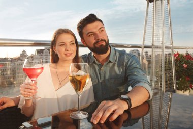 Göz kamaştırıcı bir çift bar terasında sarılıyor, gün batımında şarap içiyor, yıldönümünü kutluyor.