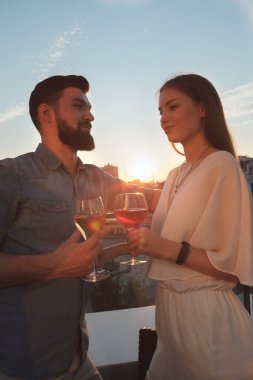 Gün batımında birlikte şarap içen genç bir çiftin dikey görüntüsü.