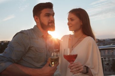 Yakışıklı sakallı adam ve güzel kız arkadaşı gün batımında şarap içiyorlar.