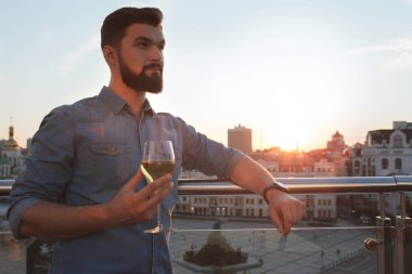 Çekici sakallı adam şehrin çatı katındaki barda gün batımını seyrediyor, şarap içiyor, fotokopi çekiyor.