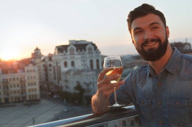 Mutlu ve yakışıklı bir adamı yakından çek, gülümse, gün batımında terasta şarap iç.