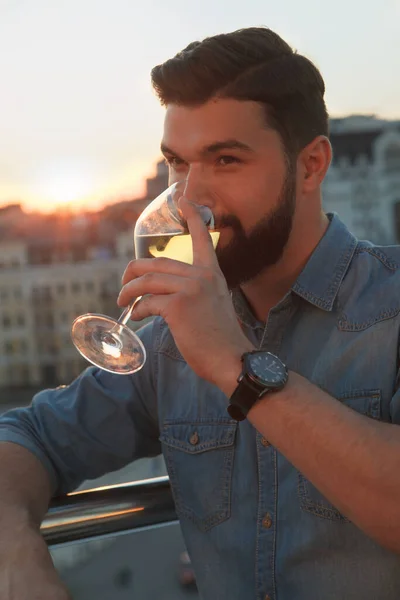 Vertical close up of a bearded man drinking wine on rooftop terrace, watching summer sunset in the city
