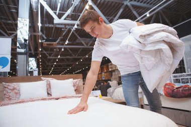 Genç adam ev eşyaları mağazasında yatak alışverişi yapıyor.