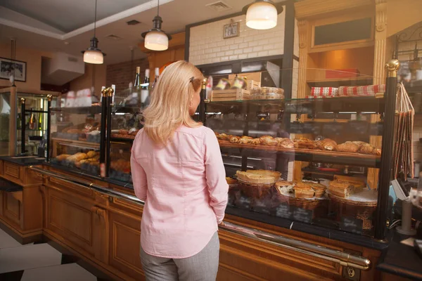 パン屋のディスプレイで販売のためのおいしいペストリーを検討している女性の顧客の背面ビューショット — ストック写真