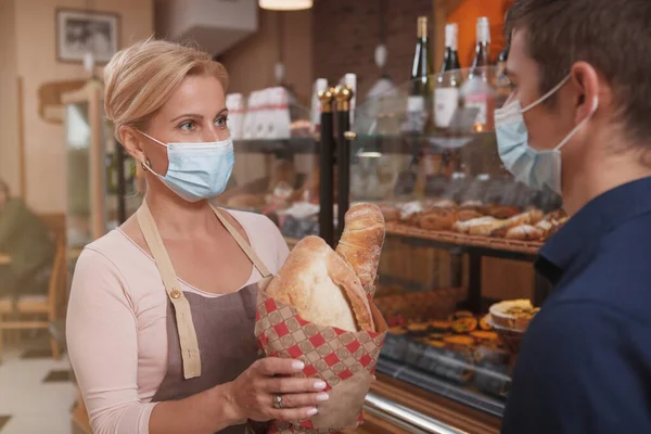 Female Baker Wearing Medical Mask While Passing Her Male Client — Stock Photo, Image