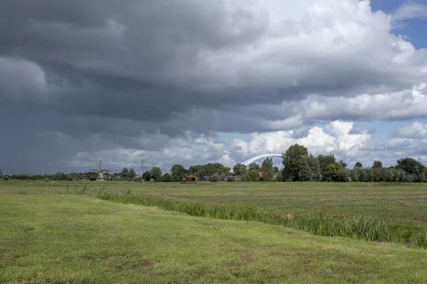 梅雨の曇り空明るい緑の牧草地 およびそれの小さなクリーク 上で地平線にオランダ風車と新しい鉄道橋オランダのアムステルダム Rijnkanaal — ストック写真