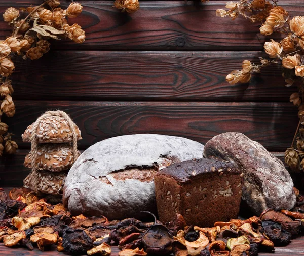 bread on a wooden background surrounded by dried fruit grain bread a bunch of ears lying next to the bread