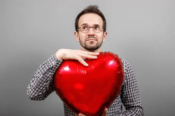 The guy on a gray background with an inflatable ball in the hands of a heart