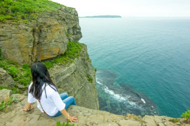 Kız bir kenarında sarp kaya denizin önce oturur ve ufukta görünüyor