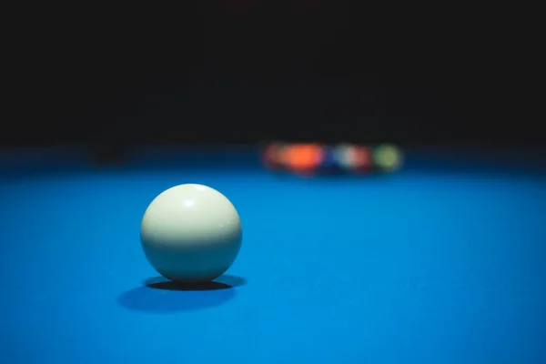 Photo of a blue pool table with a white ball down the middle in a dark room