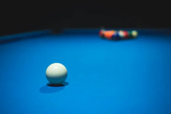 Mavi bir bilardo masasının fotoğrafı. Ortasında beyaz bir top, karanlık bir odada.