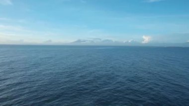 Mavi berrak su, bulutlar ve ufukta volkanlar olan deniz manzarasının videosu.