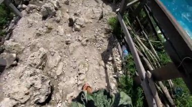 Eski bir kaya basamağındaki uygun bir insanın, yüksek bir dağdaki uçuruma deniz ve kaya manzaralı Kelingking plajındaki ilk kişi görüntüsü.