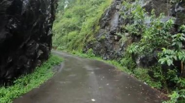 Yüksek bir dağdaki uçuruma giden bir orman yolunun, kayalı ve yeşil ağaçlı birinci şahıs videosu.
