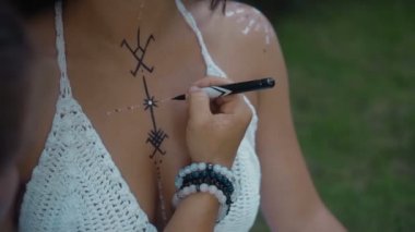 Güzel, genç, esmer, Avrupalı bir kızın videosu. Makyajlı ve vücuduna etnik çizgiler çizmiş. Tropikal bir bahçede oturuyor.