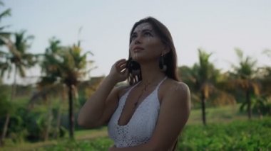 Güzel, genç, esmer Avrupalı bir kızın videosu. Makyajlı ve vücuduna etnik çizgiler çizmiş. Tropikal bir bahçede yürüyor.