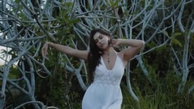 Güzel, genç, esmer Avrupalı bir kızın videosu. Makyajlı ve vücuduna etnik çizgiler çizmiş. Tropikal bir bahçede yürüyor.