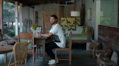 Genç, cesur Avrupalı esmer, uzun saçlı, boş bir kafede tek başına oturan, başını çevirir ve ileriye bakar, sonra kalkar ve gider.