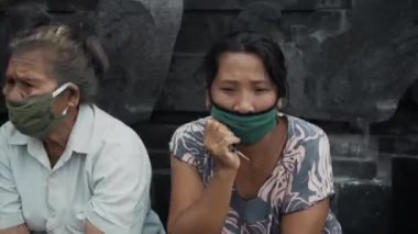 Benoa, Kuta, Kabupaten Badung, Bali, Endonezya - 8 Temmuz 2020: Yüzlerinde maskeli yaşlı insanların olduğu Endonezya 'daki küçük bir köyün videosu