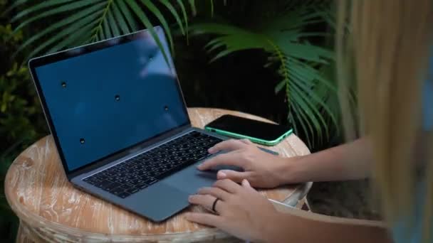 木製のテーブルに座って緑の庭でノートパソコンの後ろで働いている若い女の子のビデオ — ストック動画