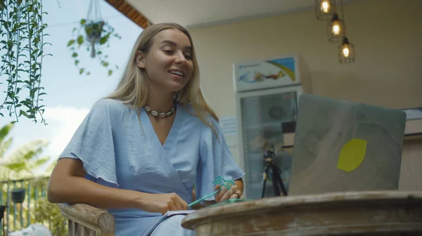 Ahşap bir masada oturan ve yeşil bir bahçede dizüstü bilgisayarın arkasında çalışan genç bir kızın fotoğrafı.