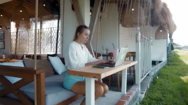 Joven Sentada Una Mesa Madera Trabajando Detrás Portátil Cafetería Tropical — Vídeo de stock