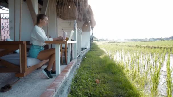 Młoda Dziewczyna Siedzi Przy Drewnianym Stole Pracuje Laptopem Tropikalnej Kawiarni — Wideo stockowe