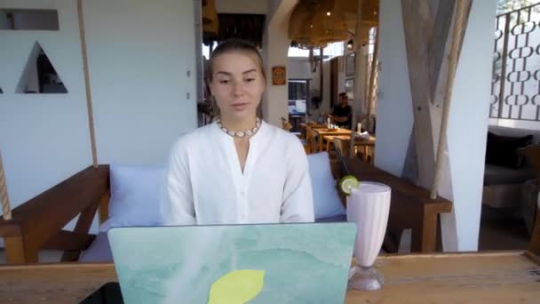 小女孩坐在一张木制桌子旁 在热带咖啡馆的笔记本电脑后面工作 — 图库视频影像
