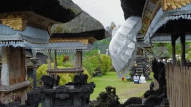 Pampatan, Rendang, Karangasem Regancy, Bali, Endonezya - 18 Temmuz 2020: Beyaz elbiseli Endonezyalı erkek, çardağı, şemsiyesi ve yeşil çimeni olan eski bir tapınağın bölgesinde dua ediyor.