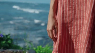 Beyaz çizgili kırmızı tişörtlü genç bir kız doğada duruyor. Arka planda bulutlar, omuzlarına hafifçe vuruyor.