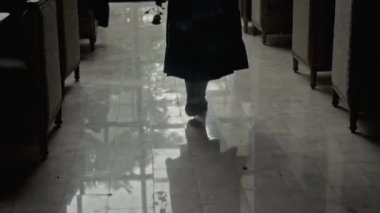 Arka bahçeye bakan büyük bir pencereye doğru yürüyen genç bir kızın silueti.