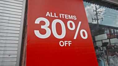 Sokakta duran kırmızı pankarttaki beyaz metin% 30 indirimli.