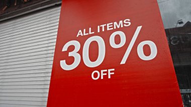 Sokakta duran kırmızı pankarttaki beyaz metin% 30 indirimli.