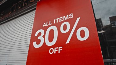 Sokakta duran kırmızı pankarttaki beyaz metin% 30 indirimli.