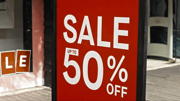 Red sign hanging on a glass window with the inscription sale up to 50% off