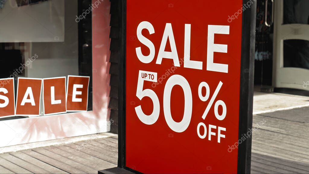 Red sign hanging on a glass window with the inscription sale up to 50% off