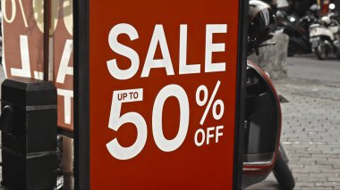 Cam bir pencereye asılı kırmızı tabela ve satışta% 50 indirim var.