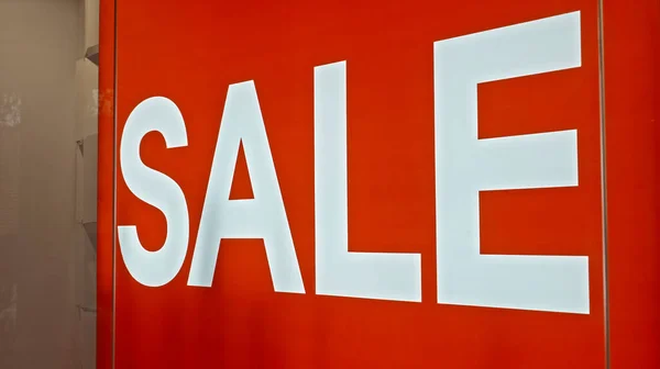White text on the red board window of the store with the inscription sale