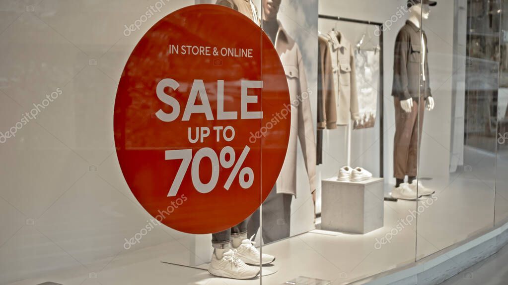 White text on the red sticker on the glass of window in the store with the inscription sale up to 70% off