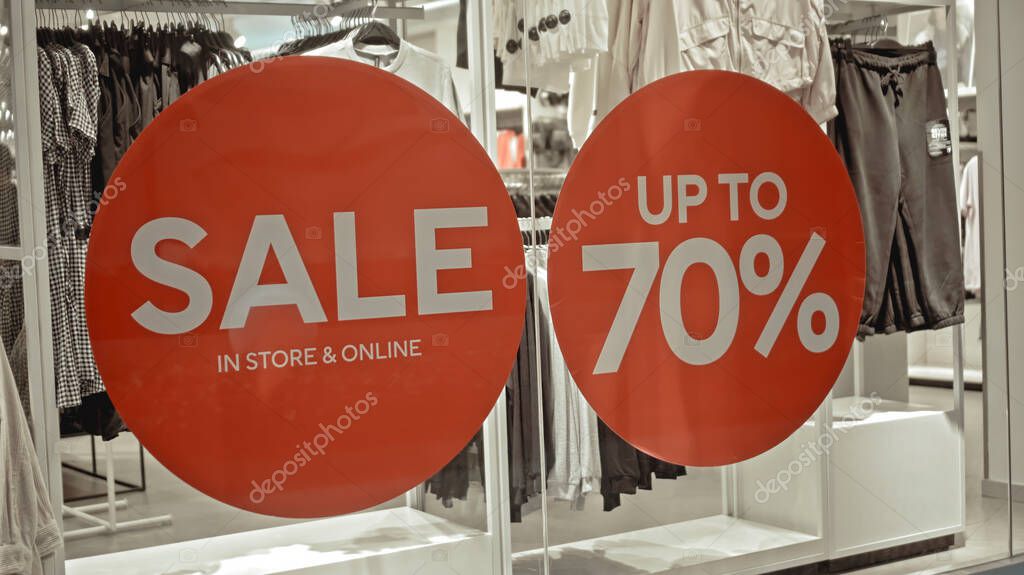 White text on the red sticker on the glass of window in the store with the inscription sale up to 70% off