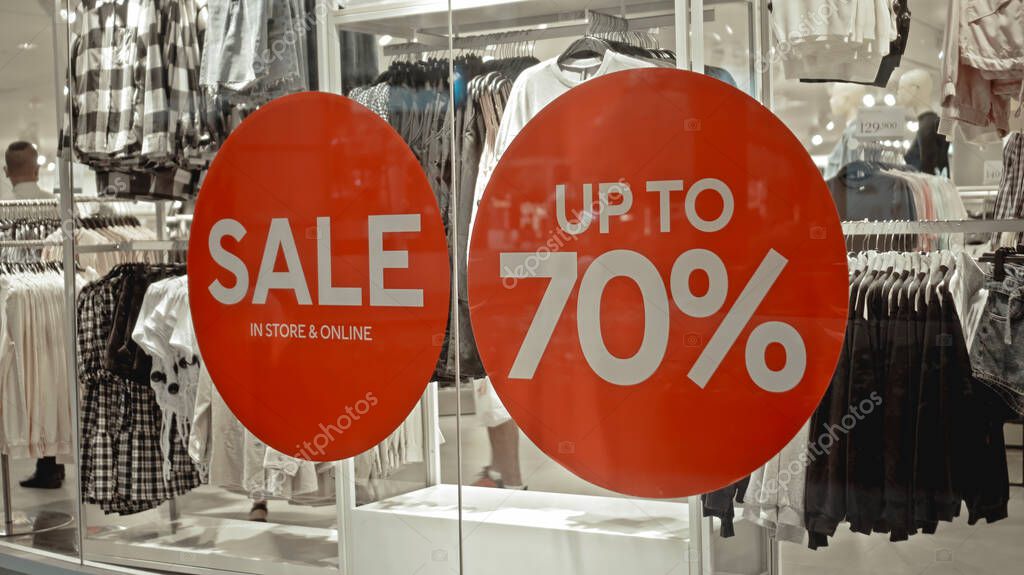 White text on the red sticker on the glass of window in the store with the inscription sale up to 70% off