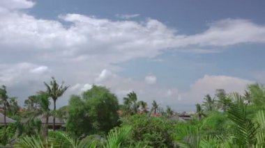 Endonezya. Yoğun bir tropikal bitki örtüsü içinde küçük bir köy. Görünümü çatılar ve bulutlar. Rüzgarlı hava. Hızlı hareket