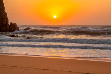 Portekiz. Cape Roca Sandy plaj. Rock ve sörf dalgalar. Arka plan açık gökyüzü ile okyanusta güneş ayarlar