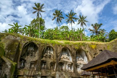 Endonezya. Bali Adası. Rock, thatched çatı ve palmiye ağaçları gökyüzü arka plan üzerinde tapınak oyulmuş