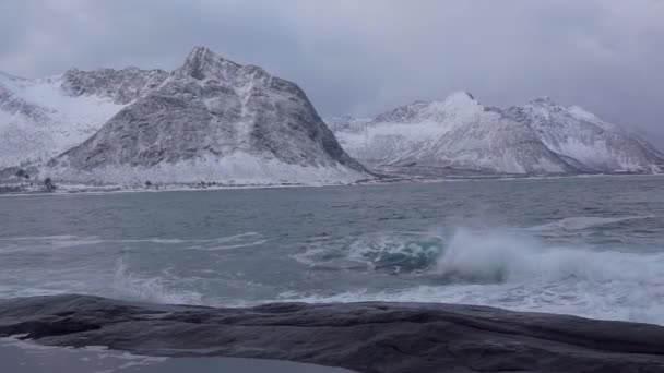 ノルウェーの北部 冬のロフォーテン諸島 曇りの夜 雪をかぶった山 岩の多い海岸 サーフィンの波 スローモーション — ストック動画
