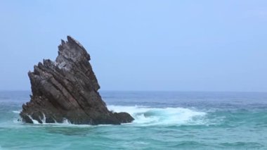 Sınırsız okyanus. Gökyüzü bulutlu. Dalga sonları kayanın üzerinde sörf