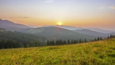 Ormanlık dağlar yaz akşamında. Çimenli glade. Tepeler ötesinde bir bulutsuz gökyüzünde güneş batacak. Zaman atlamalı