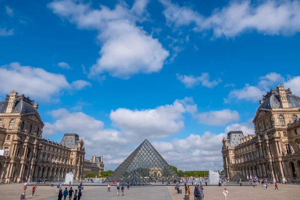 Toeristen in de piramides van het Louvre en de wolken — Stockfoto
