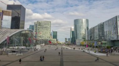 Fransa. Paris. La Defense. Yaz gecesi başlangıcı. Yaya meydanında bulutlar ve birçok insan. Zaman atlamalı