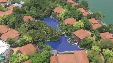 Okyanus kıyısındaki tropik tatil köyü. Bungalovların, havuzların ve birçok ağacın çatıları. Havadan görünüm